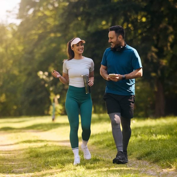 Happy athletic couple communicating while walking in nature after sports training. Copy space.